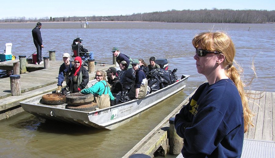 Profile of Stephanie on the shore with folks on Jon boat with trash