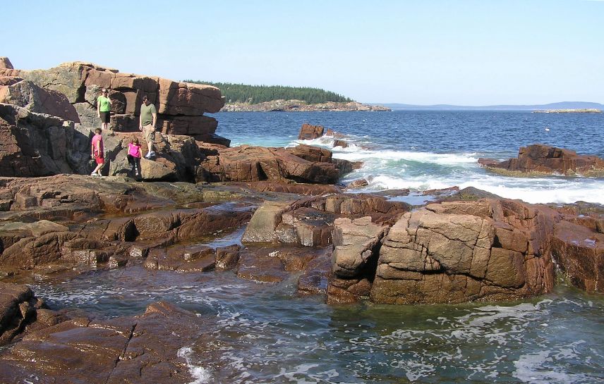 Big wet rocks by the water with a family walking on them