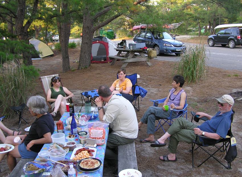 Group sitting around campsite enjoying potluck meal