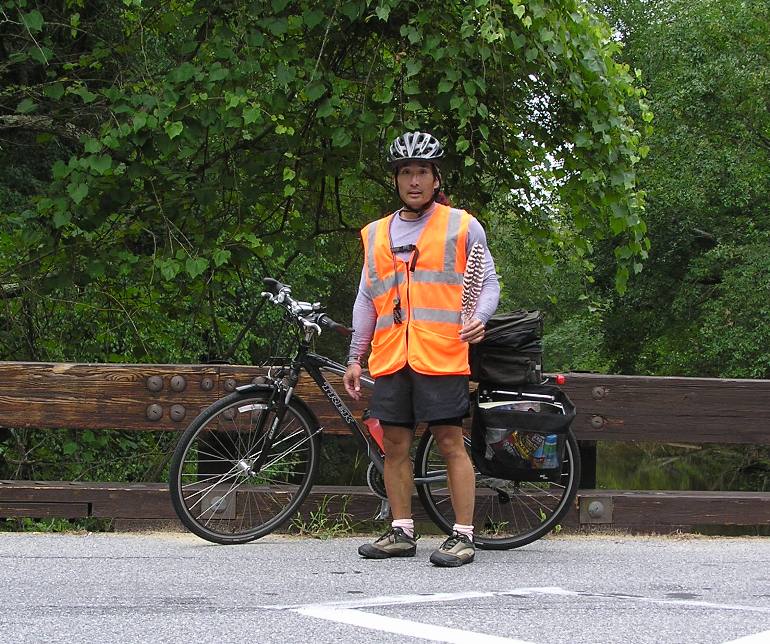 Me wearing orange vest next to my bicycle and holding an osprey feather