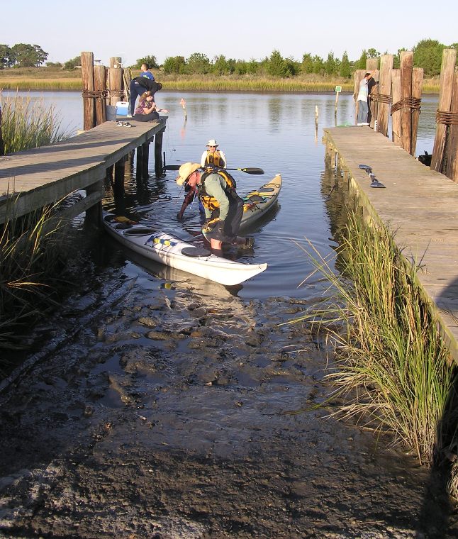 Kayakers taking out their boats at a muddy ramp