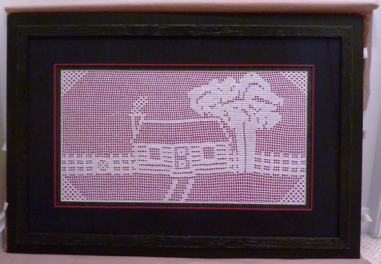 Glass-framed hand-sewn picture of a house