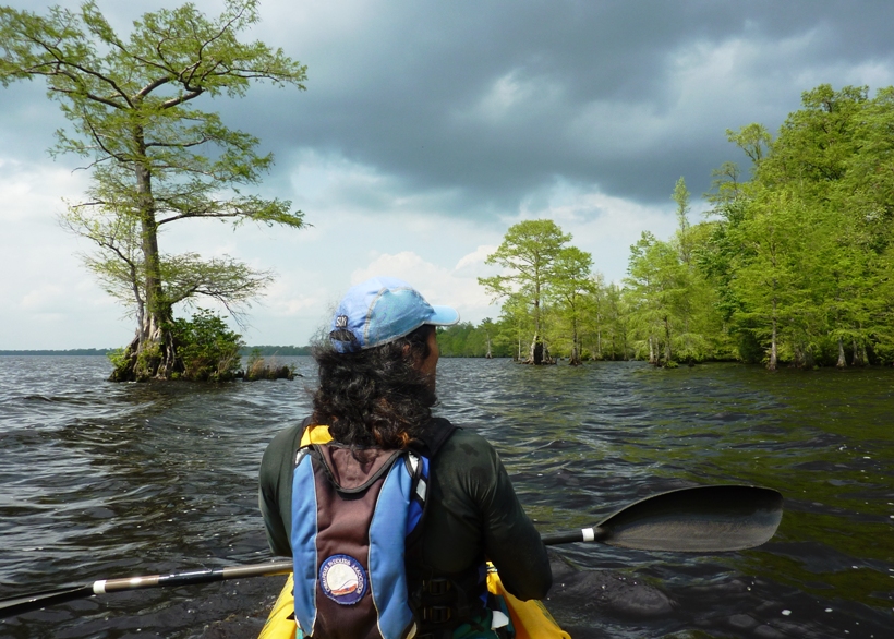 Me on kayak with strong wind blowing my hair and cypress trees in background