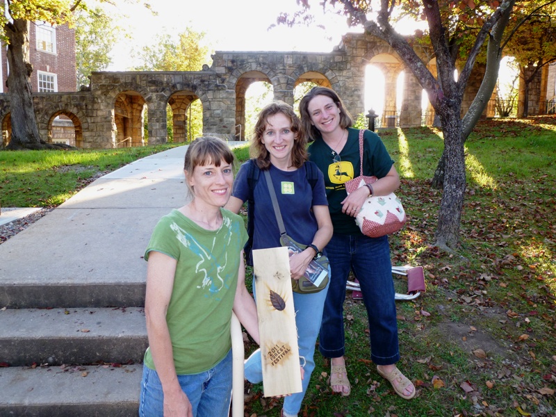 Joyce, Norma, and Laah holding wood with event logo