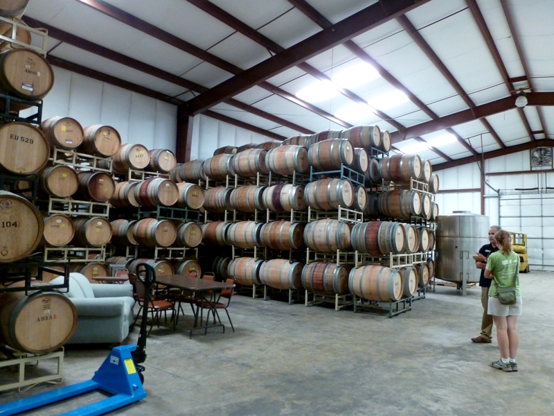 Norma talking to guy at winery in space full of barrels