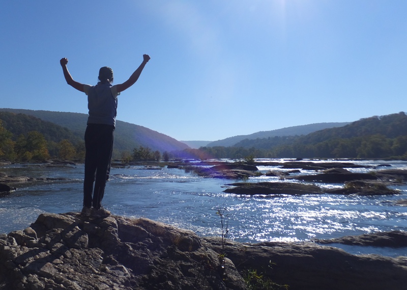 Carmen standing on a rock with both arms raised