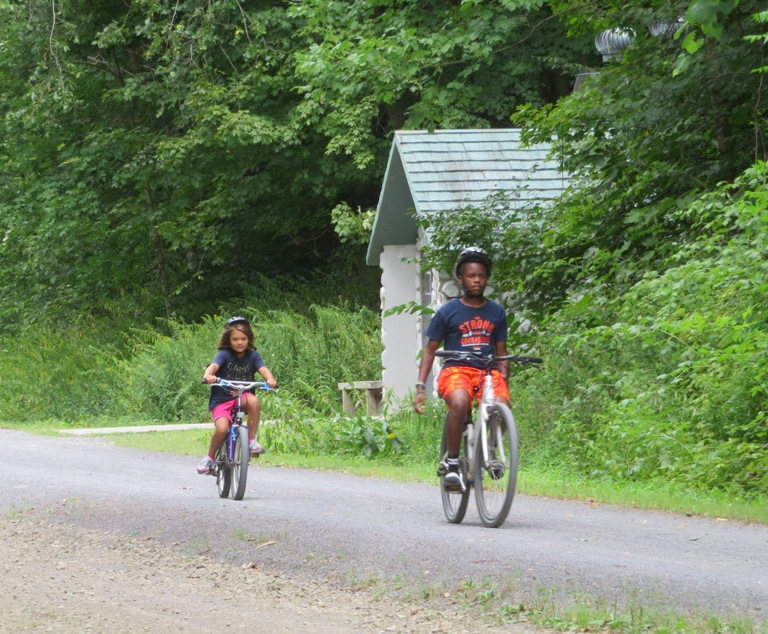 Two kids riding, the older one without his hands on the handlebars