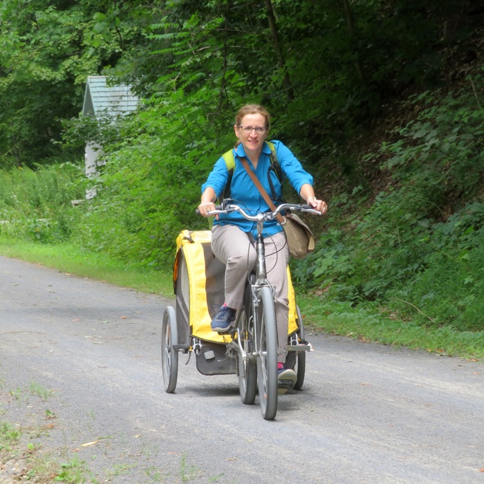 Norma biking, pulling a trailer with the youngest child