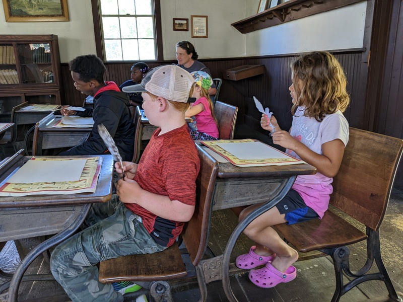 Kids in classroom practicing penmanship with feather quill pens