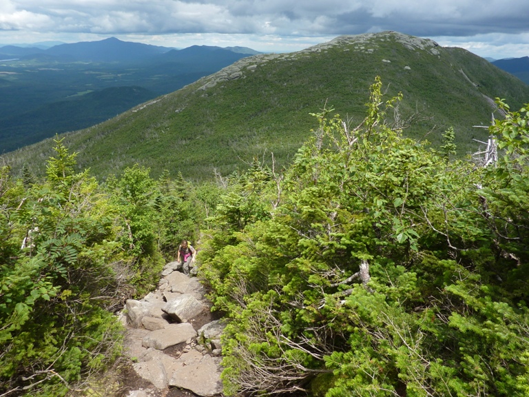 Norma scrambling up rocks in the sun with cloudy mountains behind