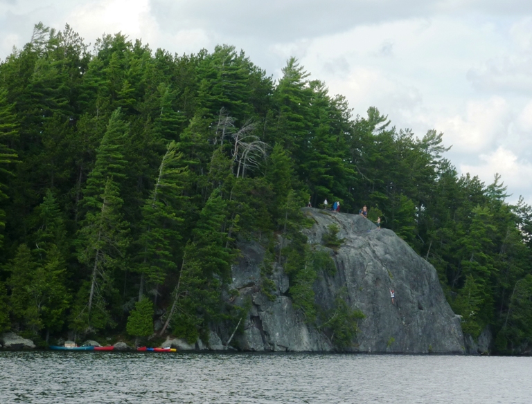 People at the top of a cliff with someone climbing up the side