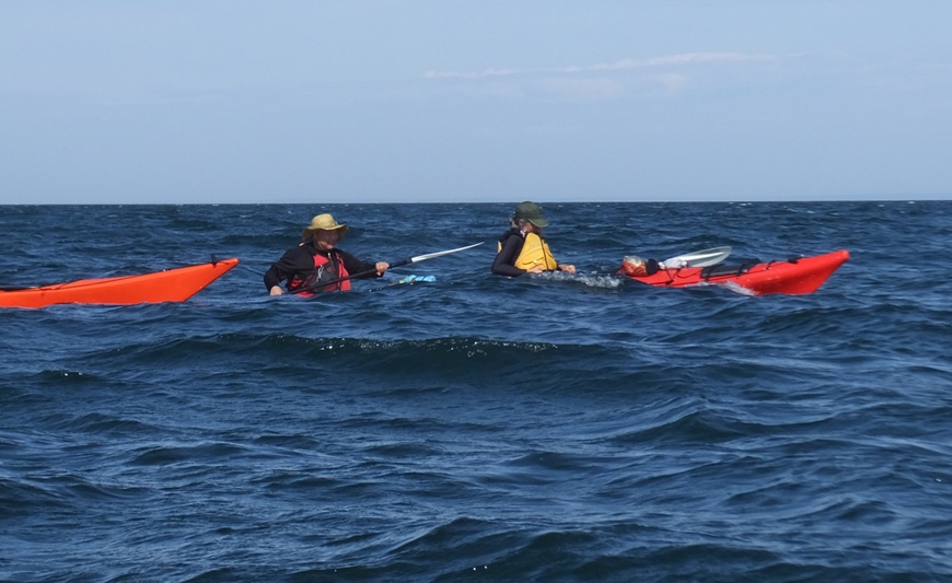 Steve and Carmen in their kayak with a wave hiding most of their boat