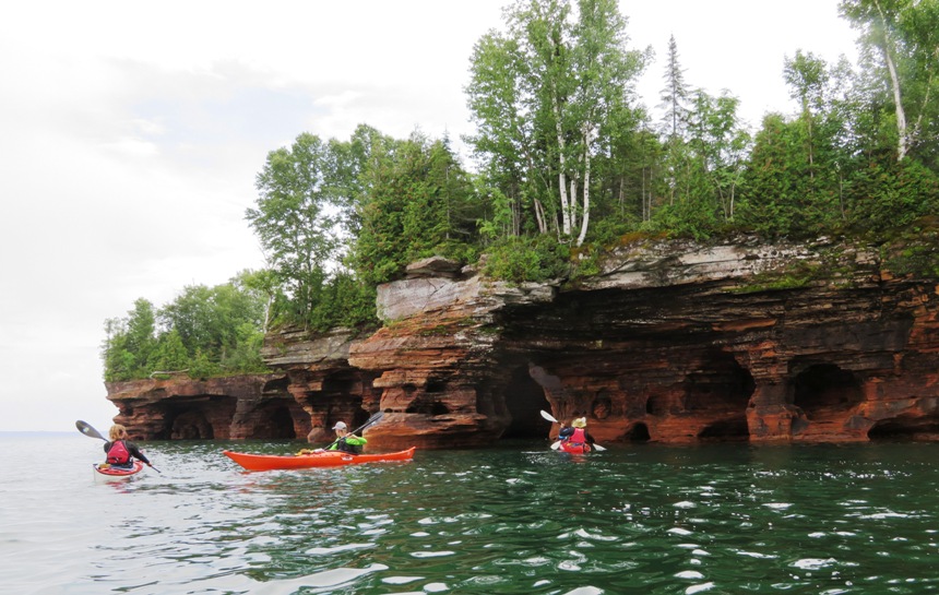 Zoomed out view of kayakers, caves, and vegetation on top