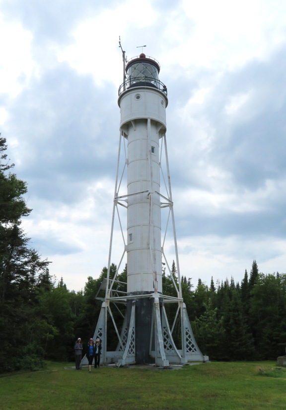 White painted Devils Island lighthouse with three people standing at the bottom