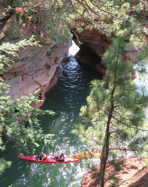 Kayakers with light shining through opening in rocks