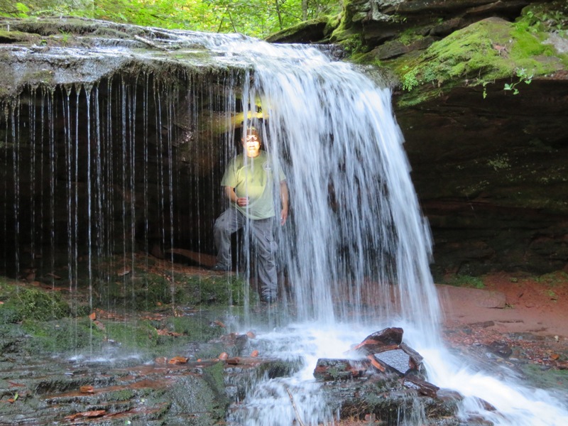 Steve shining a flashlight on himself from behind the waterfall