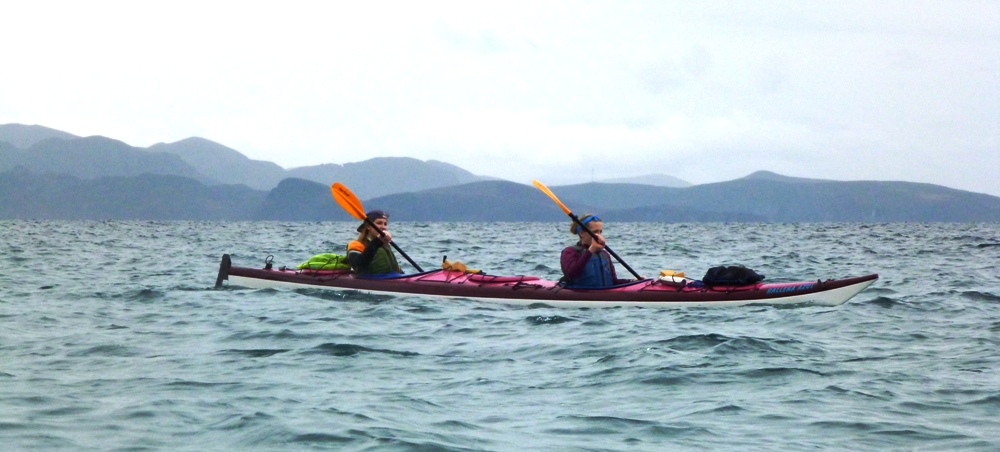 Leah and Kim in a tandem kayak with rolling hills behind