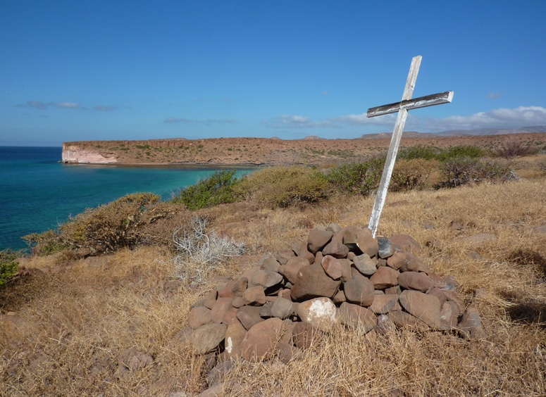 Big white cross propped up by rocks.  Water in the distance