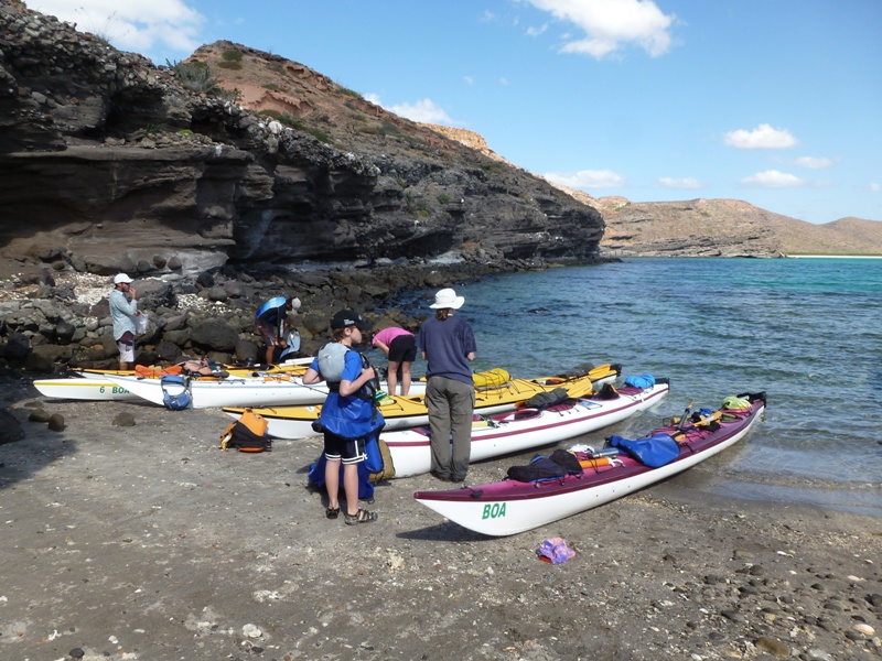 Small beach at Punta Prieta with dark rocks, kayaks, and people