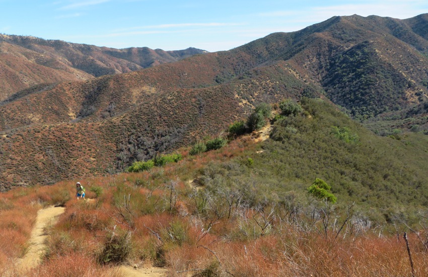 Norma walking on trail with mountains behind