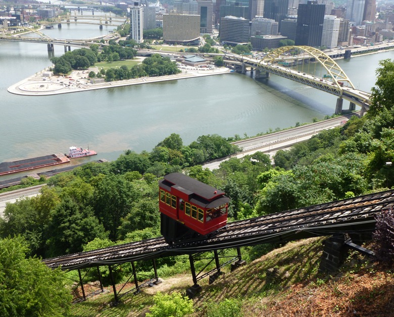 Trolley-like vehicle on steep incline with view of city below