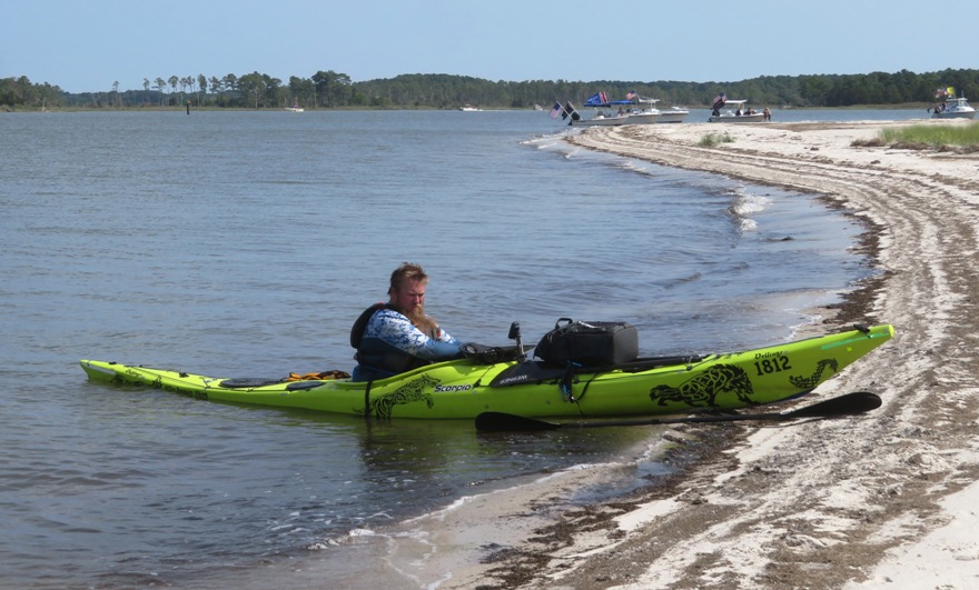 Nate in kayak with power boats behind flying Trump flags