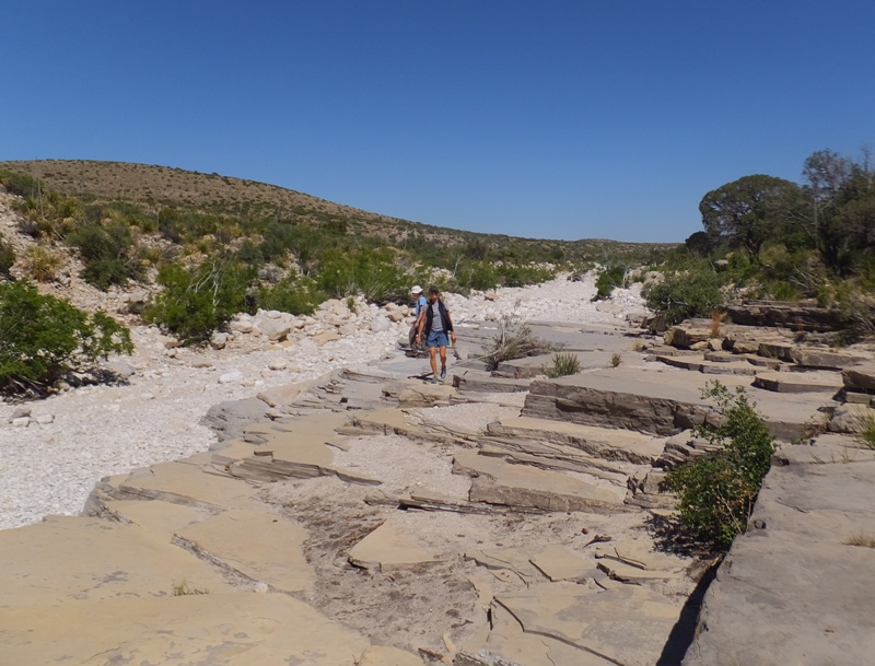 Norma and Carmen walking on large, flat rocks that border the dry riverbed