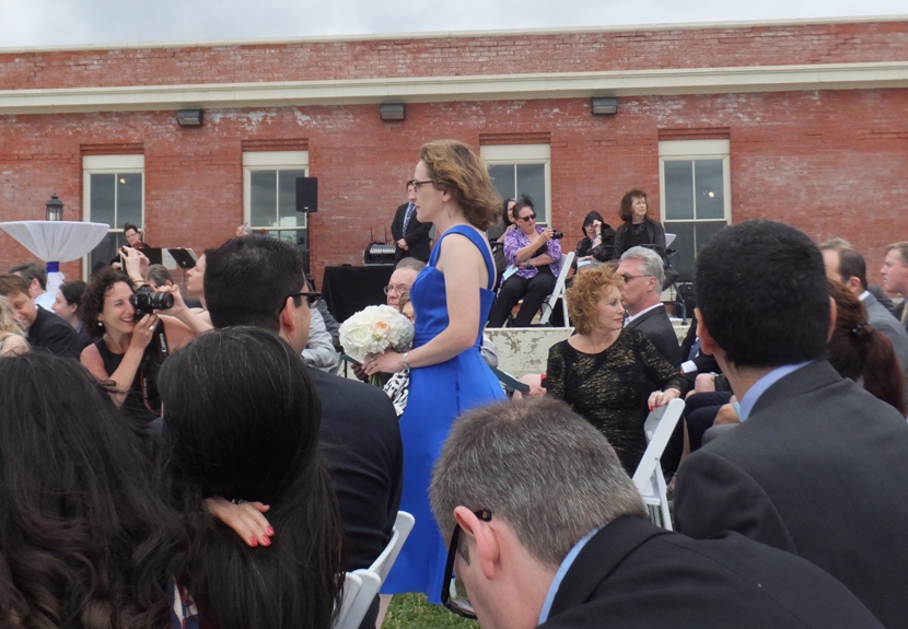 Norma in blue dress, carrying white flowers