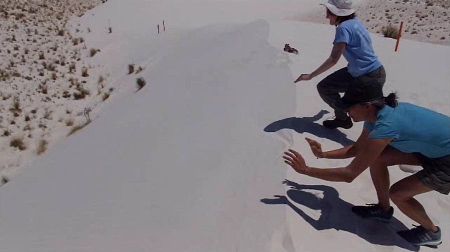 Video of Norma and Carmen sliding down a dune on their bellies