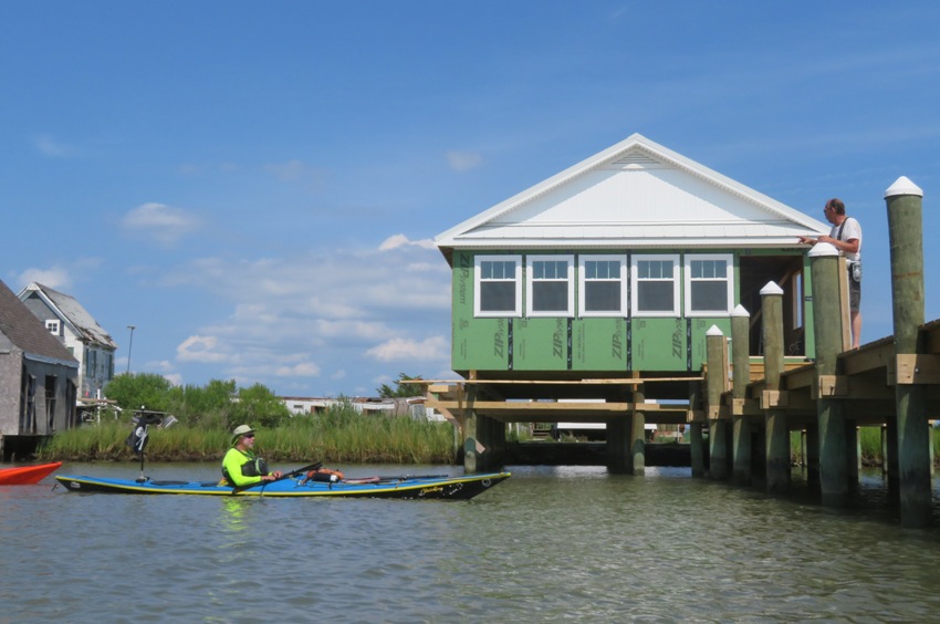 Greg in kayak talking to man on pier with house behind that is being repaired