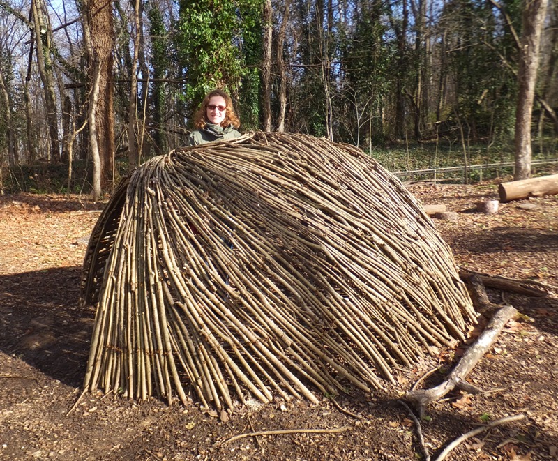 Norma sticking her head out of the top of a woven twig structure resembling an igloo