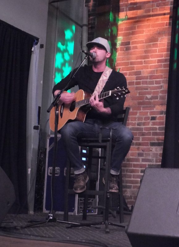 Casey Derhak playing guitar and singing while seated