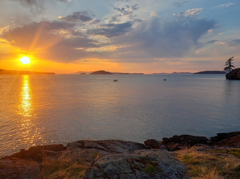 View of the sun low in the sky with kayakers in the distance