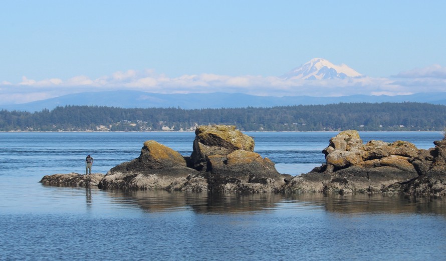 Me standing on a rocky peninsula looking into the water with Mount Baker behind