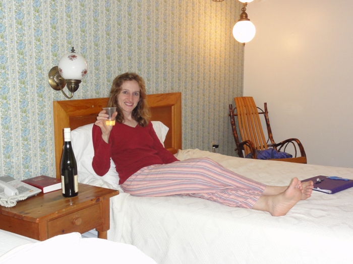 Norma holding a glass of wine in bed