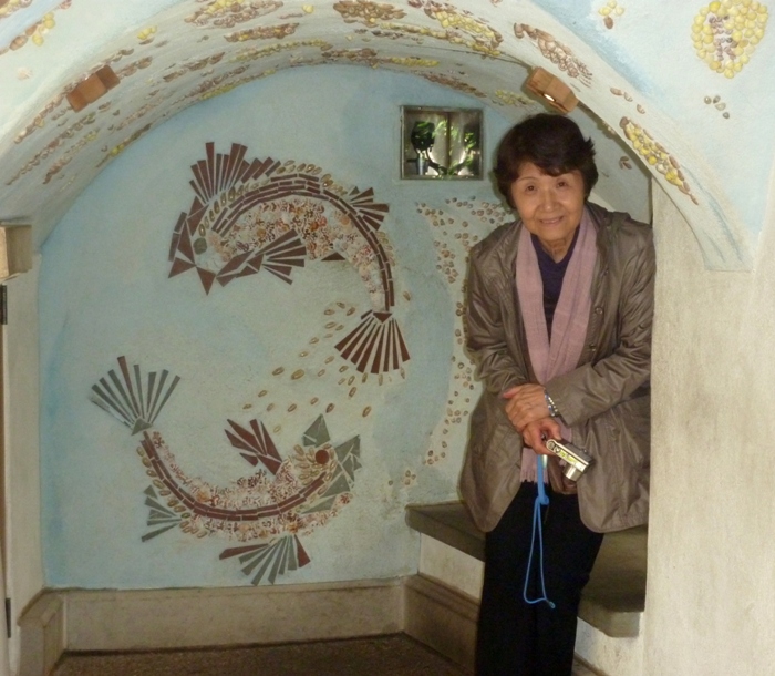 Hitomi with shells, rocks, and cut tiles create pictures on the walls