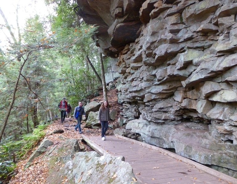 People walking on boardwalk by craggy vertical rock wall