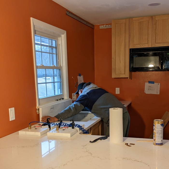 Machine joining together two large pieces of quartz with guy behind installing backsplash below window