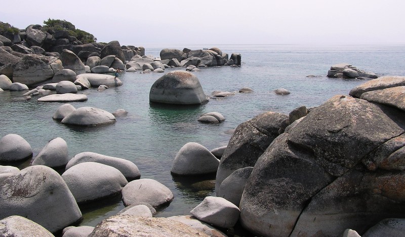 Numerous boulders in the water with a guy on a rock, ready to dive into the lake