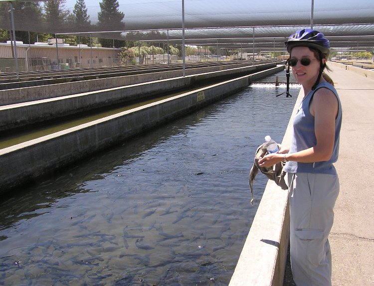 Norma with bicycle helmet standing next to water full of fish