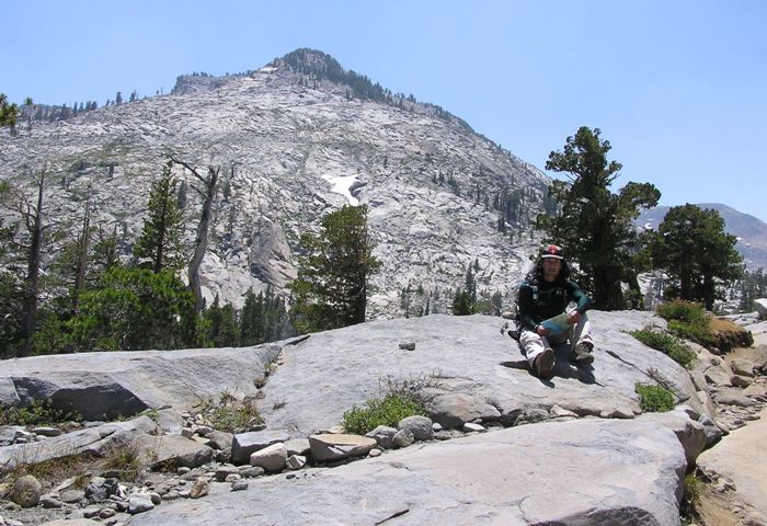 Me sitting on a rock with a rocky mountain behind.  It has some snow