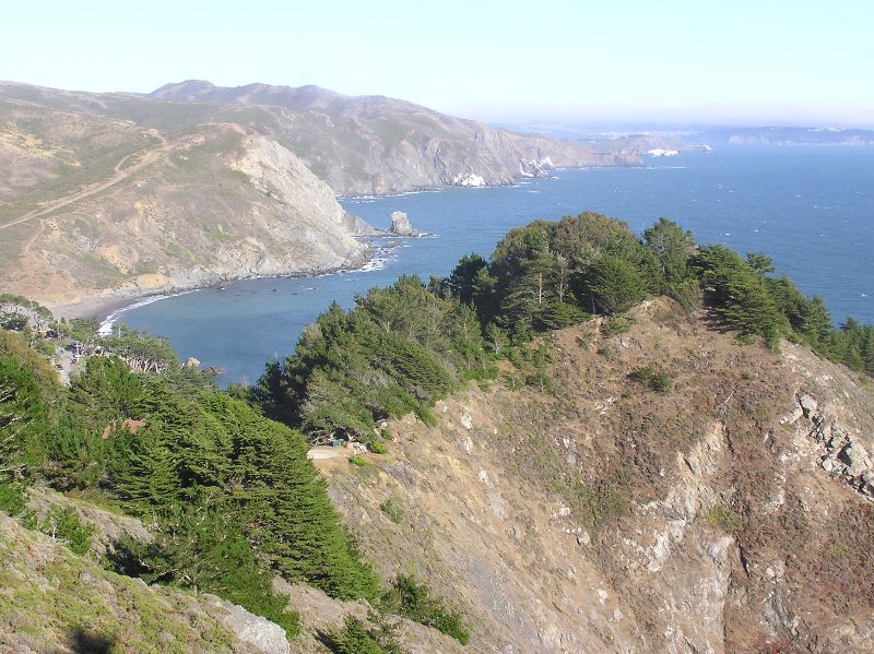 Steep, rugged cliffs by water with wooded area in front