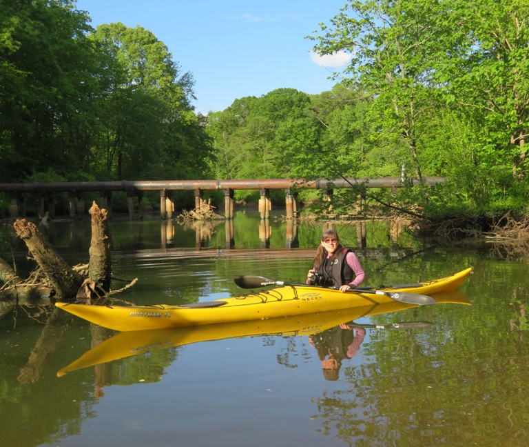 Sara on her kayak with some big, elevated, horiztal pipe behind her