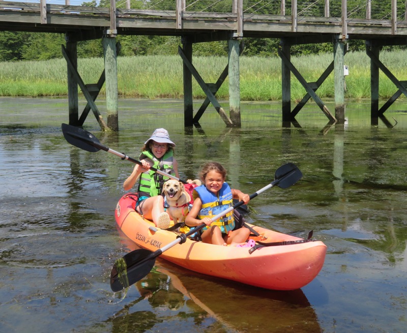 Norma, Alisha, and Daphne in kayak with pedestrian bridge behind