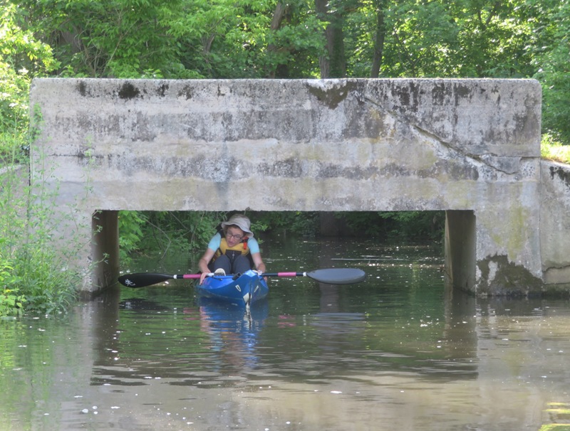 Norma leaning forward in kayak to fit under road