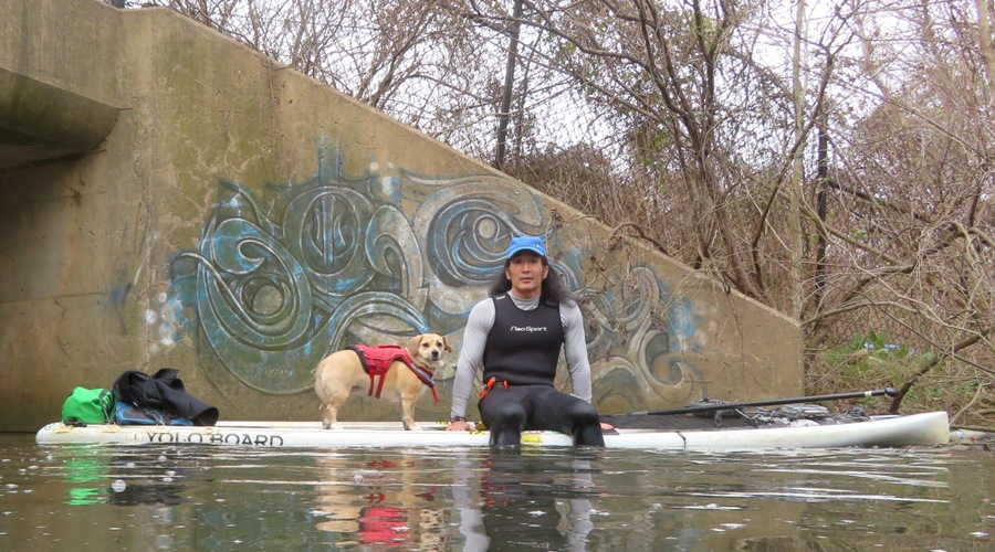 Me sitting on the SUP and Daphne standing, on the opposite side of Highway 895, with graffiti on a wall behind